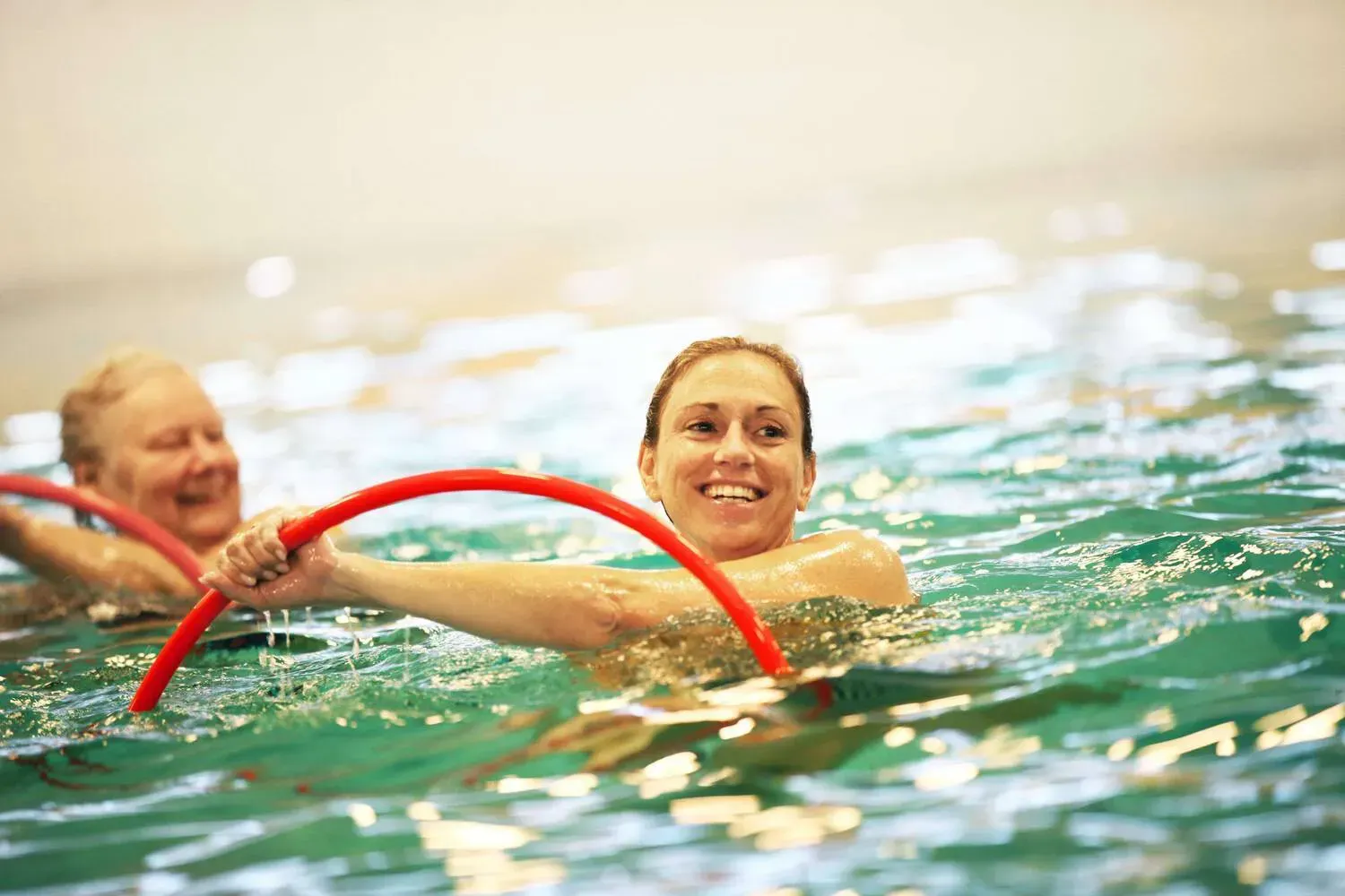 lachende vrouw met bril in het zwembad met blauw/gele gewichten in haar handen